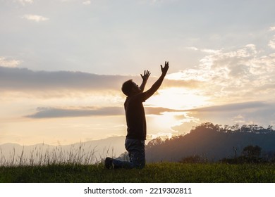 Young male kneeling down with hands open palm up praying to God on the mountain sunset background.  - Shutterstock ID 2219302811