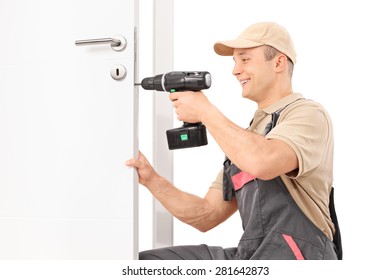 Young Male Locksmith Screwing A Screw On A Lock Of A Door With A Hand Drill Isolated On White Background