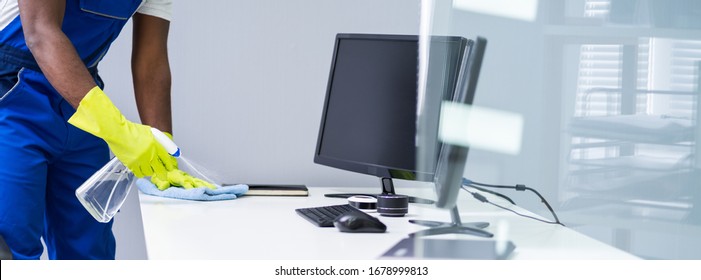 Young Male Maid Cleaning Glass Desk With Feather Duster In Office