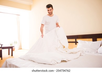 Young Male Is Making Bed In Hotel Room.