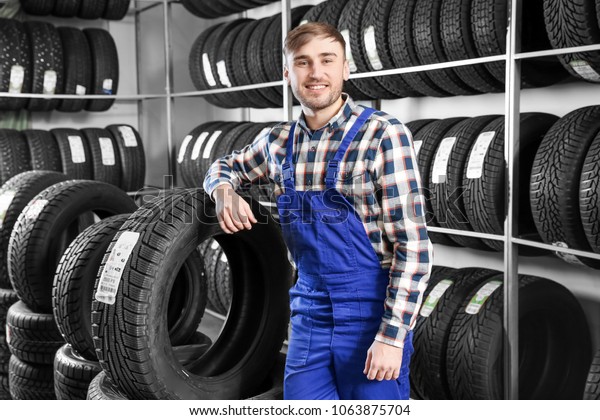 Young male mechanic with car tires in automobile\
service center