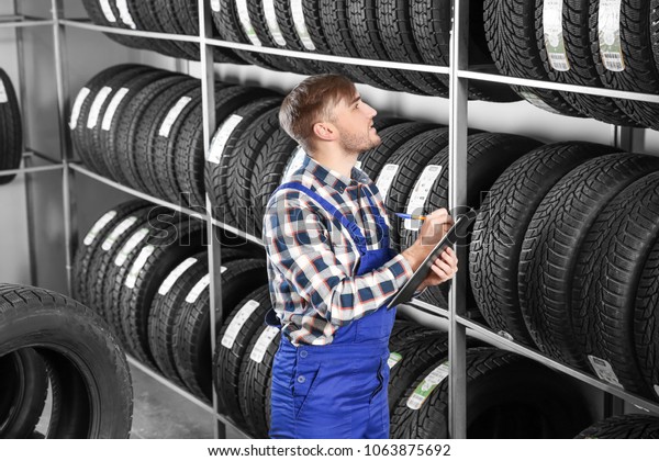 Young male mechanic with clipboard near tires in\
automobile service center