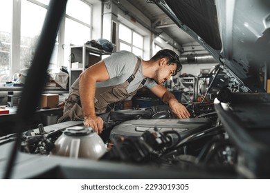 Young male mechanic examining engine under hood of car at the repair garage - Powered by Shutterstock