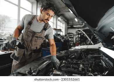 Young male mechanic examining engine under hood of car at the repair garage - Powered by Shutterstock