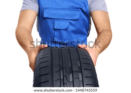 Young male mechanic in uniform with car tire on white background, closeup