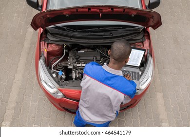 Young Male Mechanic Using Laptop While Examining Car Engine