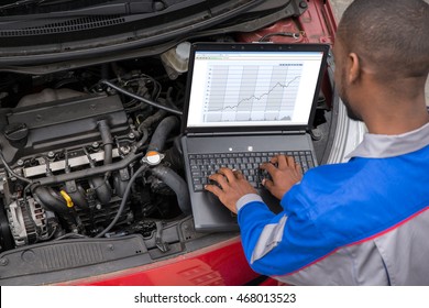 Young Male Mechanic Using Laptop While Examining Car Engine