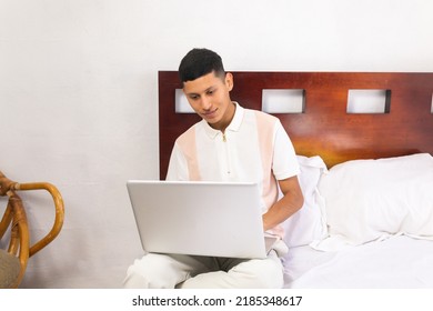 Young Male Mexican Student Using Laptop Sitting On Bed