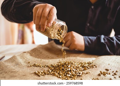 Young Male Miner Sitting At Table And Pouring Gold Out Of Glass Jar