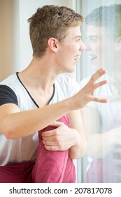 A Young Male Model Is Pressing His Nose Against His Own Reflection In A Window And Touching It With His Hands