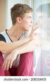 A Young Male Model Is Pressing His Nose Against His Own Reflection In A Window And Touching It With His Hands. He Does Not Like Himself!