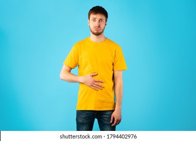 Young male model touching his stomach, feeling satiety after eating hearty meal, having good appetite