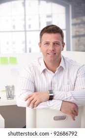 Young Male Office Worker Sitting On Chair Conversely In Office, Smiling.?