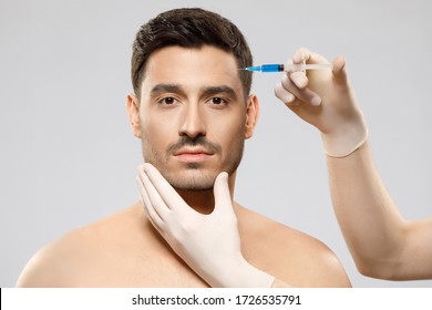 Young male, patient of beautician, receiving filler injection into forehead zone, willing to look younger, taking care of skin, isolated on gray background. Plastic surgery concept