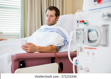 Young male patient using mobilephone at dialysis center, waiting for treatment