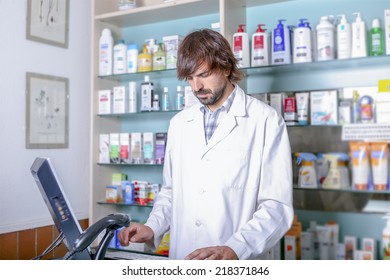 Young Male Pharmacist Using The Computer In The Pharmacy Standing