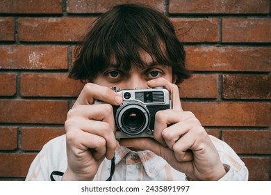 Young male photographer captures city life through lens of old retro classic film camera at brick wall background - Powered by Shutterstock