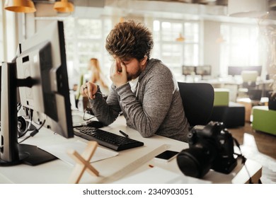 Young male photographer editing photos on his computer while working from the office - Powered by Shutterstock