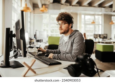 Young male photographer editing photos on his computer while working from the office - Powered by Shutterstock