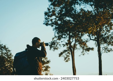 Young male photographer standing and taking photos on the mountain, background view of mountains and clouds, sunset. - Powered by Shutterstock