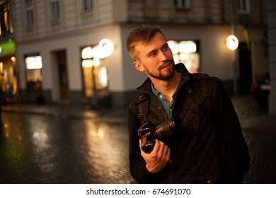 Young Male Photographer Stands On City Street In Evening. In Background There Are Night City Lights. Self-portrait.