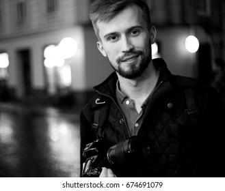 Young Male Photographer Stands On City Street In Evening. In Background There Are Night City Lights. Black And White Image. Self-portrait.