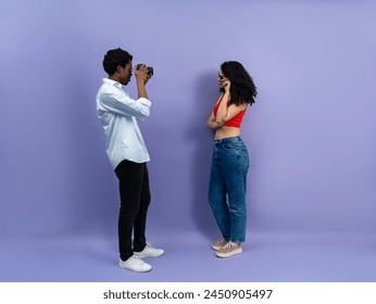 Young Male Photographer Taking Photo Of Female Model In Casual Outfit Against Purple Background - Powered by Shutterstock