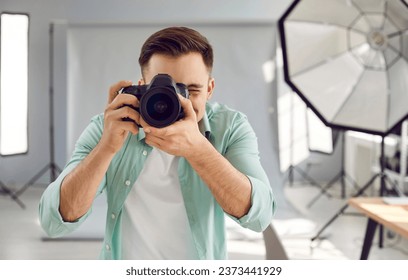 Young male photographer taking photos with dslr camera. Front view shot of handsome photographer shooting in studio with digital camera and professional lighting equipment - Powered by Shutterstock