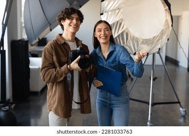 Young male photographer talking with female art director, talking and preparing for photo shooting, woman pointing forwards and smiling, standing near modern lighting equipment - Powered by Shutterstock