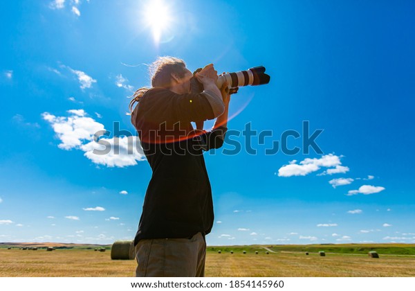 Young male photographer with telephoto lens\
attached to DSLR camera shooting towards the sky in a bright sunny\
day. Copy space on top, lens\
flares