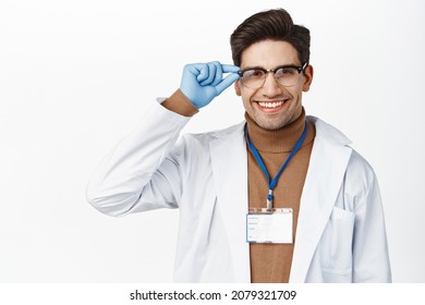 Young Male Physician, Medical Scientist In Glasses And Rubber Gloves, Smiling And Looking Happy At Camera, Standing In Medical Robe Over White Background