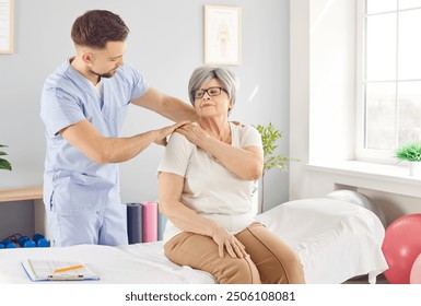 Young male physiotherapist, chiropractor or osteopath helps senior woman with spine problems. Manual therapy specialist working with old patient with back or neck pain during rehabilitation in clinic. - Powered by Shutterstock