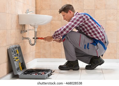 Young Male Plumber Fitting Sink With Wrench In Bathroom
