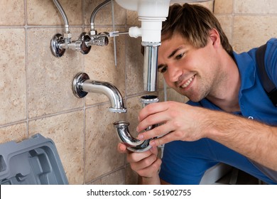 Young Male Plumber Fitting Sink Pipe In Bathroom