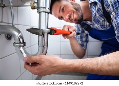 Young Male Plumber Repairing Sink With Adjustable Wrench In Bathroom - Powered by Shutterstock