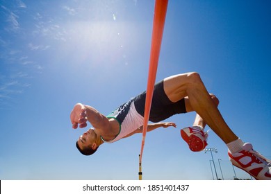 Young male pole vaulter jumping over a bar during a practice session at the track on a bright, sunny day with a clear blue sky in the background