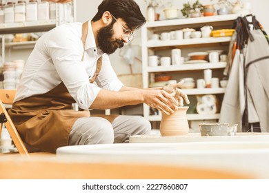 A young male potter is engaged in craft in his workshop on a potter's wheel and makes a clay product - Powered by Shutterstock