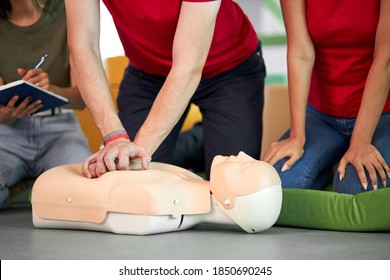 young male practicing CPR first aid on a mannequin in the presence of people, indoors - Powered by Shutterstock