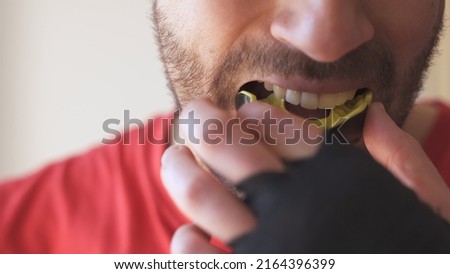 Young male putting mouthguard before boxing sparring training