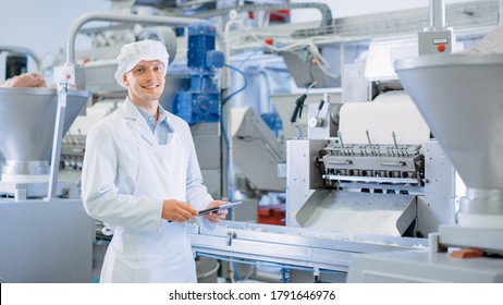 Young Male Quality Supervisor Or Food Technician Is Inspecting The Automated Production At A Dumpling Food Factory. Employee Uses A Tablet Computer For Work. He Looks To The Camera And Smiles.