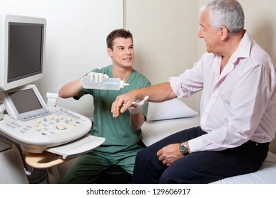 Young male radiologic technician looking at patient while putting gel on his hand