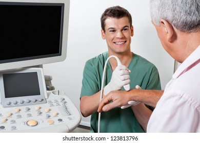 Young male radiologic technician smiling while scanning male patient's hand at clinic