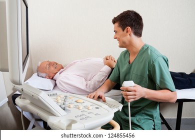 Young male radiologic technician smiling while looking at senior patient