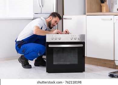 Young Male Repairman Repairing Oven In Kitchen