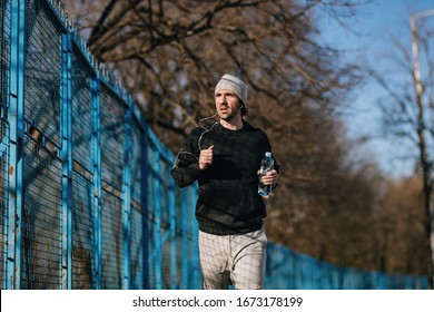 Young Male Runner Carrying Bottle Of Water While Jogging In The Park. 