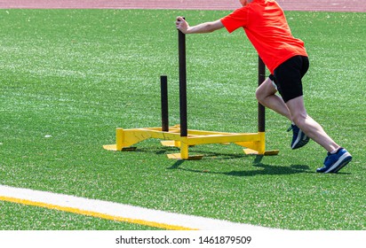 A Young Male Runner Is Pushing A Yellow Sled On A Green Turf Field At Running Camp.