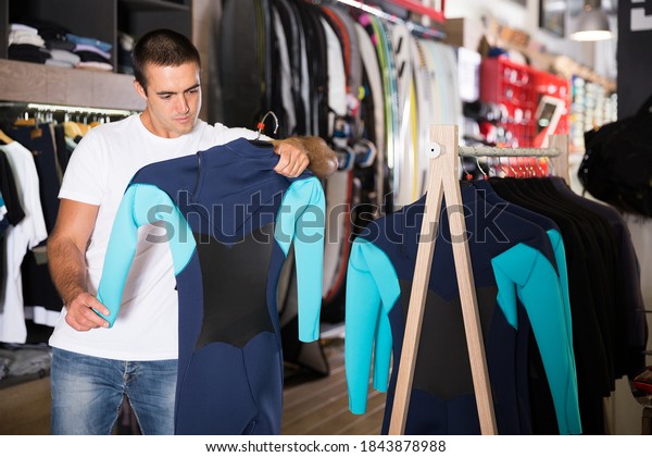 Young male shopper looking for new wetsuit during\
shopping in store
