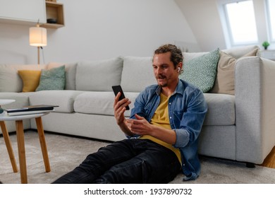 Young male sitting on the floor in the living room and having video call via phone - Powered by Shutterstock