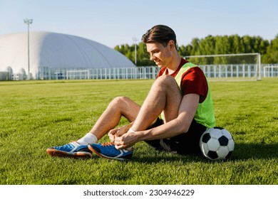 Young male soccer player tying shoelace on football field - Powered by Shutterstock