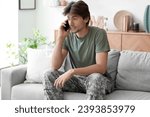 Young male soldier talking by mobile phone while sitting on sofa at home